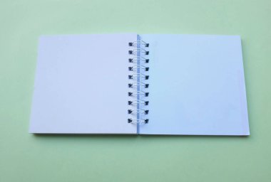 Üst ve düz yatıyordu boş boş beyaz spiral not defteri yeşil pastel arka plan izole. Ofis veya eğitim ekipmanları.