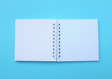 Üst ve düz uzanan boş boş beyaz spiral not defteri mavi bir arkaplanda izole edilir. Ofis veya eğitim ekipmanları.