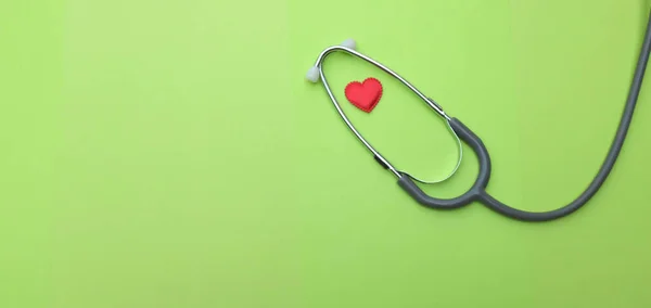 Yeşil masaya yatırılmış kırmızı kalp beyaz steteskop. Doktor masası. Sağlık konsepti..