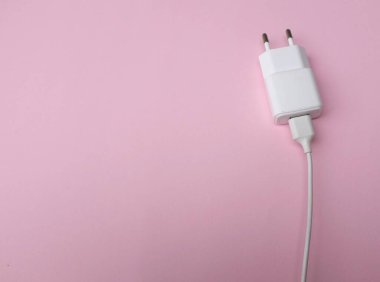 Üst görünüm ve düz konum şarj adaptörü Pembe pastel arka plan üzerinde beyaz akıllı telefon rengi