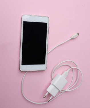 Üst ve düz yatıyordu beyaz akıllı telefon fişi Pembe pastel arka plan şarj adaptörü ile