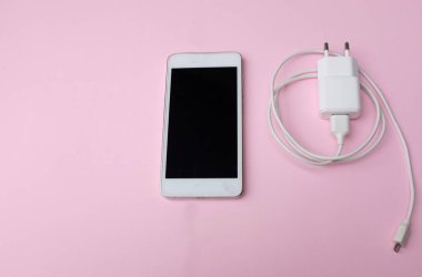 Üst ve düz yatıyordu beyaz akıllı telefon fişi Pembe pastel arka plan şarj adaptörü ile