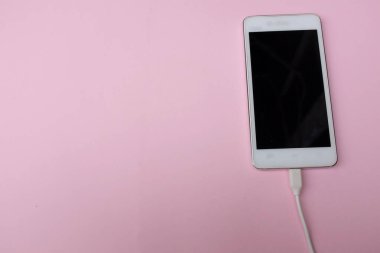 Pembe pastel arkaplan üzerine şarj adaptörü takılı beyaz akıllı telefonu kopyala