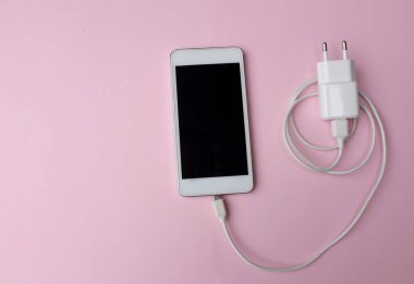 Üst ve düz yatıyordu beyaz akıllı telefon fişi Pembe pastel arka plan şarj adaptörü ile