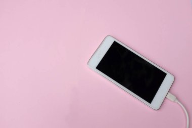 Üst ve düz yatıyordu beyaz akıllı telefon fişi Pembe pastel arka plan şarj adaptörü ile