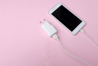 Pembe pastel arkaplan üzerine şarj adaptörü takılı beyaz akıllı telefonu kopyala