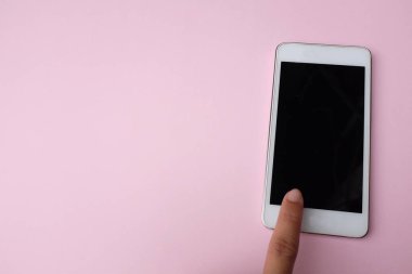 Üst görünüm ve düz uzanma pembe pastel arka planda akıllı telefona dokunuyor