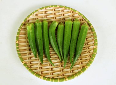 young raw okra, ladys finger, gombo, gumbo, bendee, quimbamto (hisbicus esculentus l.) vegetables In a bamboo tray .flat lay