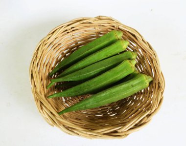 young raw okra, ladys finger, gombo, gumbo, bendee, quimbamto (hisbicus esculentus l.) vegetables In a bamboo rattan basket .flat lay
