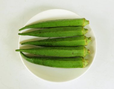 young raw okra, ladys finger, gombo, gumbo, bendee, quimbamto (hisbicus esculentus l.) vegetables On the plate .flat lay