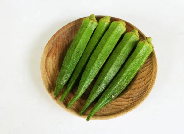 young raw okra, ladys finger, gombo, gumbo, bendee, quimbamto (hisbicus esculentus l.) vegetables On the wooden plate .flat lay