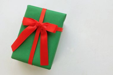 Kırmızı kurdeleli yeşil hediye kutusu beyaz arka planda.