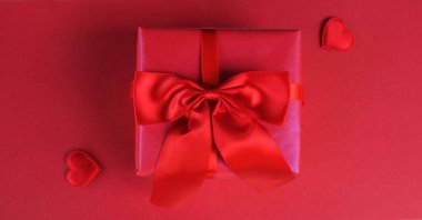 Kırmızı kurdeleli pembe bir hediye kutusu ve kırmızı zemin üzerinde kırmızı bir kalp.