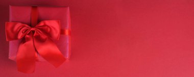 Kırmızı arkaplanda kırmızı kurdeleli pembe bir hediye kutusu.