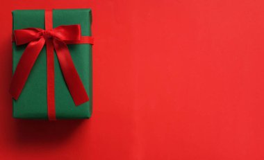 Kırmızı arkaplanda kırmızı kurdeleli yeşil bir hediye kutusu.
