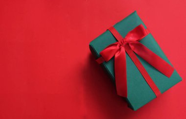 Kırmızı arkaplanda kırmızı kurdeleli yeşil bir hediye kutusu.