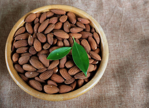 top view a heap of brown raw almonds nuts in a wooden bowl on linen fabric isolated on white backdrop