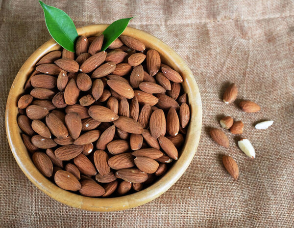 top view a heap of brown raw almonds nuts in a wooden bowl on linen fabric isolated on white backdrop