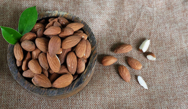 a heap of brown raw almonds nuts in a wooden bowl on linen fabric isolated on white backdrop