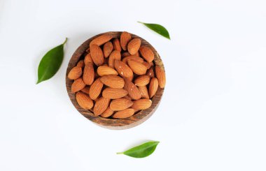 Üst manzara kahverengi badem yığını ahşap bir kasede fındık ve yeşil yaprak beyaz zemin üzerinde izole