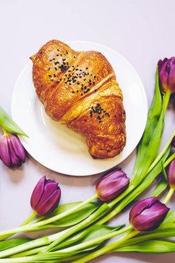 Kıtır taze kruvasan ve arka planda mor laleli kahve. Fransız kruvasanı. Yemek deseni. Fransız kahvaltısı. Üst Manzara. Yumuşak seçici odak.