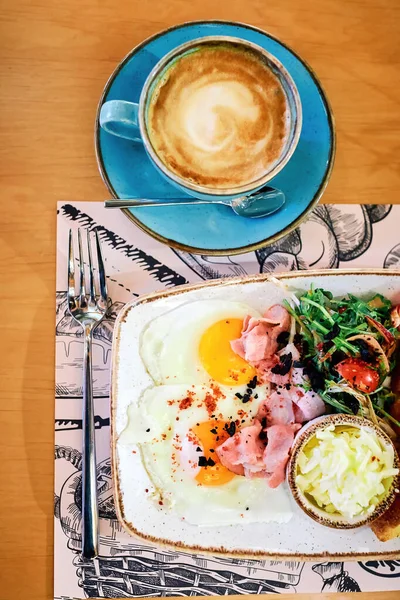 Full American Breakfast. top view. Sunny side fried eggs, salad, butter, roasted bacon, toasts and coffee for breakfast.