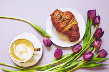 Kıtır taze kruvasan ve arka planda mor laleli kahve. Fransız kruvasanı. Yemek deseni. Fransız kahvaltısı. Üst Manzara. Yumuşak seçici odaklanma. Çiçek deseni