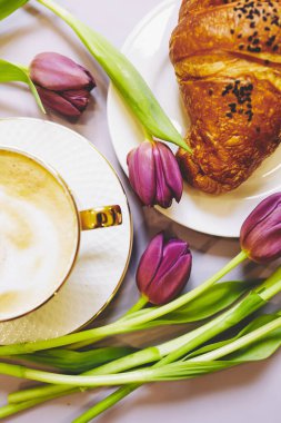 Kıtır taze kruvasan ve arka planda mor laleli kahve. Fransız kruvasanı. Yemek deseni. Fransız kahvaltısı. Üst Manzara. Yumuşak seçici odaklanma. Çiçek deseni