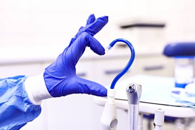 Tükürük püskürtücü ve tek kullanımlık eldivendeki bir el dişçide aşkı simgeler. Mavi bir eldiven verin. Mavi salya püskürtücü. Diş muayenehanesinin atmosferi. Diş hekiminde aşkla..