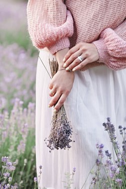 Lavanta çiçeği tutan güzel bir el. Kadınların elleri yüzükler ve kolye takıyor modern aksesuarlar zarif bir yaşam tarzı. Seçici odak ve sanat tahılı 