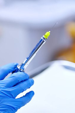 Dişçinin elinde lokal anestezi için şırınga var. 