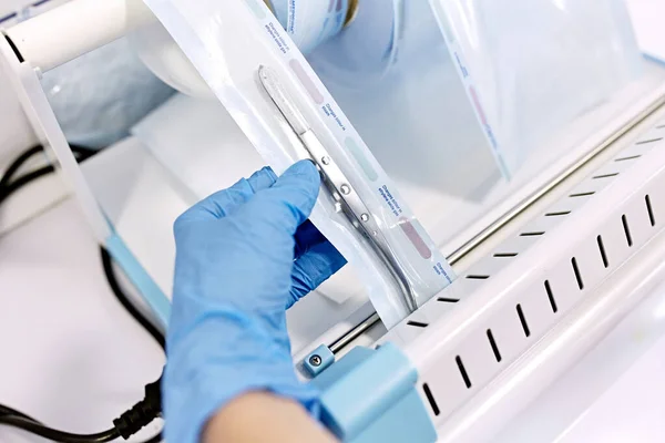 Sterilizing box. Sterilization of instruments. Dentist tools. Sterilization procedure. Hands in blue gloves holding dentist tools.