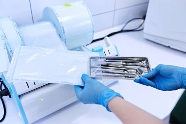 Sterilize etme kutusu. Aletlerin sterilizasyonu. Dişçi aletleri. Sterilizasyon prosedürü. Mavi eldivenli eller dişçi aletleri tutuyor..