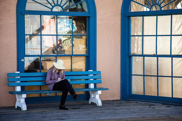 Woman reading on a bench in front of reflective windows