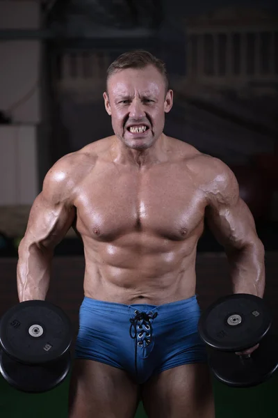 一个男人在体育馆里参加体育运动 锻炼他的肌肉 健美运动员是用哑铃练功的 — 图库照片