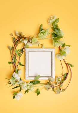 Ranunculus çiçekleriyle süslenmiş güzel boş antika çerçevenin düz kompozisyonu, dokulu sarı duvarda. Bir menü, resepsiyon, parti posteri veya düğün davetiyesi için metin kopyala. 