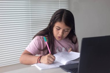 Not defterine yazan küçük bir kız. Evde dizüstü bilgisayarla ödev yapıyor. Yeni normal