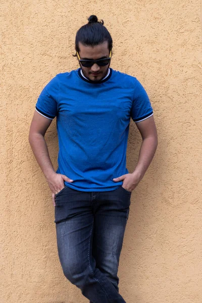 マスタード色の壁を見下ろして立ってポケットにサングラスと手を持つ若いラテン系の男 新鮮なコンセプト — ストック写真