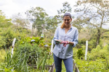 Sebze bahçesinde elinde bahçe aletleri tutan bir kadın.