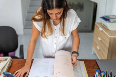 Masasının önünde duran bir kadın. Büyük, açık bir kitap çevirme sayfası.