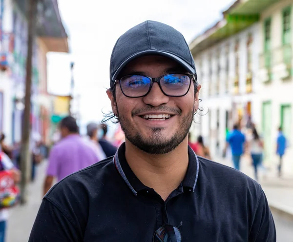 Retrato riéndose joven latino con gorra y anteojos en una calle de un pueblo en Filandia Quindio — Foto de Stock