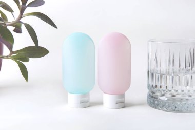 Kozmetik ürünleri için pembe ve mavi tüpler beyaz arka plan görünümünde su ve çiçek bardakları bir yana