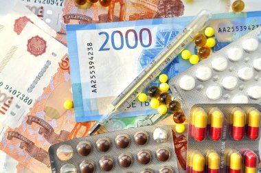 İlaç, vitamin, gıda takviyesi, hap ve para resimleri. Fotoğrafta ilaç tabletleri ve paranın üzerine yayılmış bir termometre var..