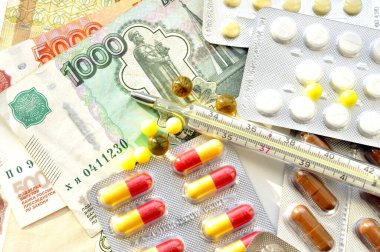 İlaç, vitamin, gıda takviyesi, hap ve para resimleri. Fotoğrafta ilaç tabletleri ve paranın üzerine yayılmış bir termometre var..