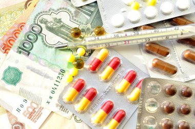 İlaç, vitamin, gıda takviyesi, hap ve para resimleri. Fotoğrafta ilaç tabletleri ve paranın üzerine yayılmış bir termometre var..