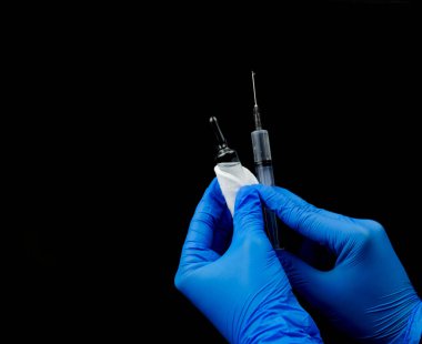 Mavi eldivenli eller şırıngayla pamuklu bir ampul tutuyor..