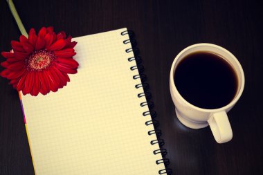 Kırmızı gerbera çiçek, fincan kahve ve ahşap des notebook