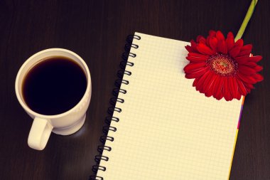 Kırmızı gerbera çiçek, fincan kahve ve ahşap masanın üstünde defter