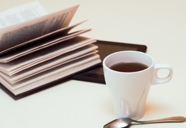 Beyaz fincan çay, dijital tablet ve kaşık hafif ahşap masa