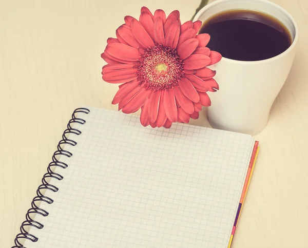Pembe gerbera çiçek, fincan kahve ve ahşap des notebook